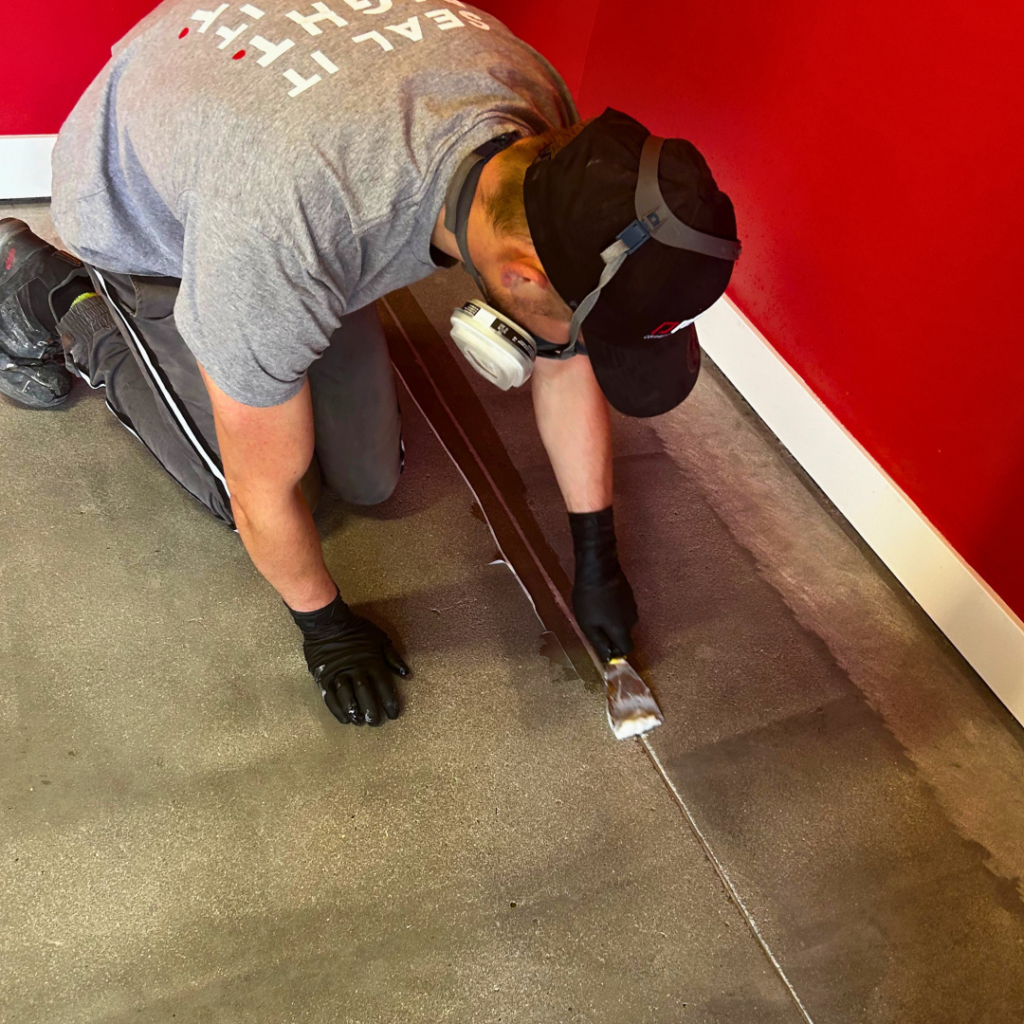 A man filling a crack in a concrete floor before preparing it for sealer application.